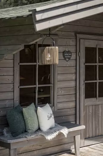 Kleine Holzhütte mit Bank, Lampe und drei Polster