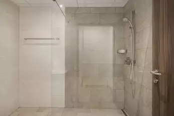 große moderne Dusche mit beigen Fließen und großem Schutzglas