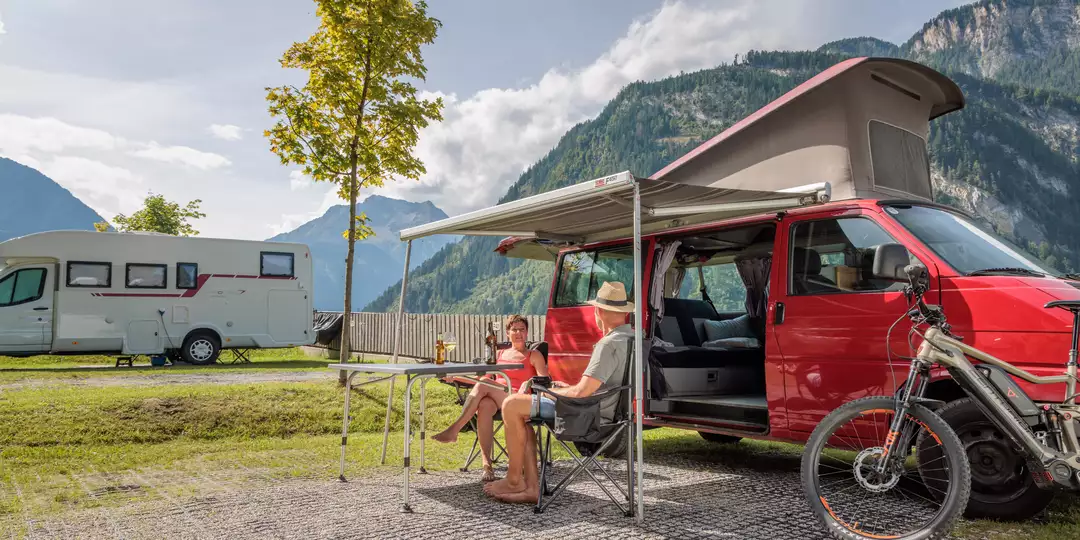 Campen im Sommer © becknaphoto - Thomas Eberharter Paar sitzt vor einem roten Camper an einem Campingtisch