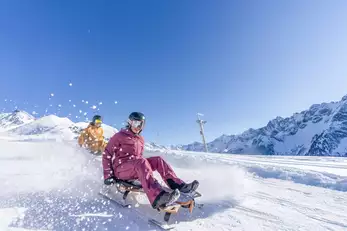 Zwei Menschen rodeln auf einer Rodelbahn