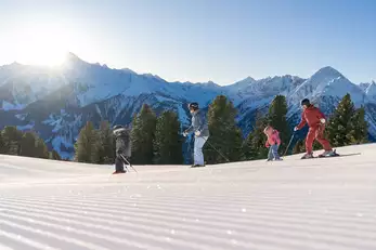 Familie mit zwei kleinen Kindern sind auf einer frisch präparierten Piste beim Skifahren