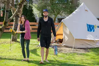 zwei Erwachsene tragen Kletterequipment durch den Campingplatz
