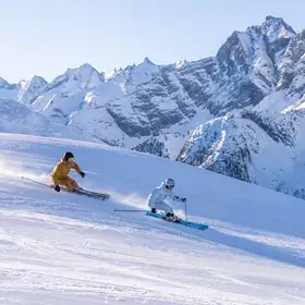 Zwei Skifahrer fahren auf präparierter Piste mit Bergpanorama