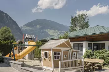 großer Kinderspielplatz mit Schaukeln, Rutschen und kleinem Holzhaus
